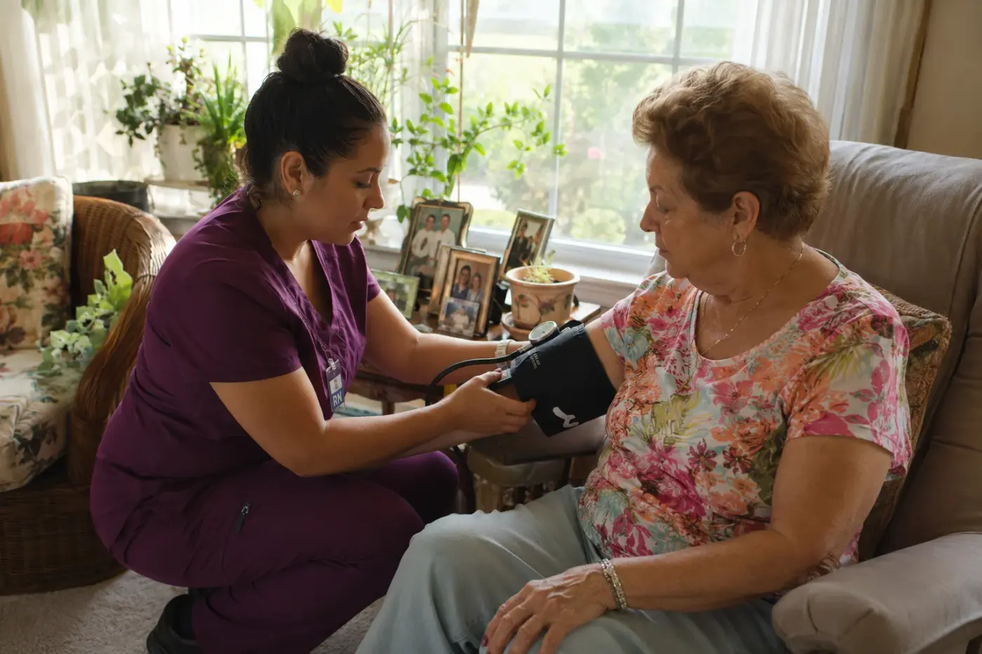 A caregiver checks an older woman's blood pressure in her living room.
